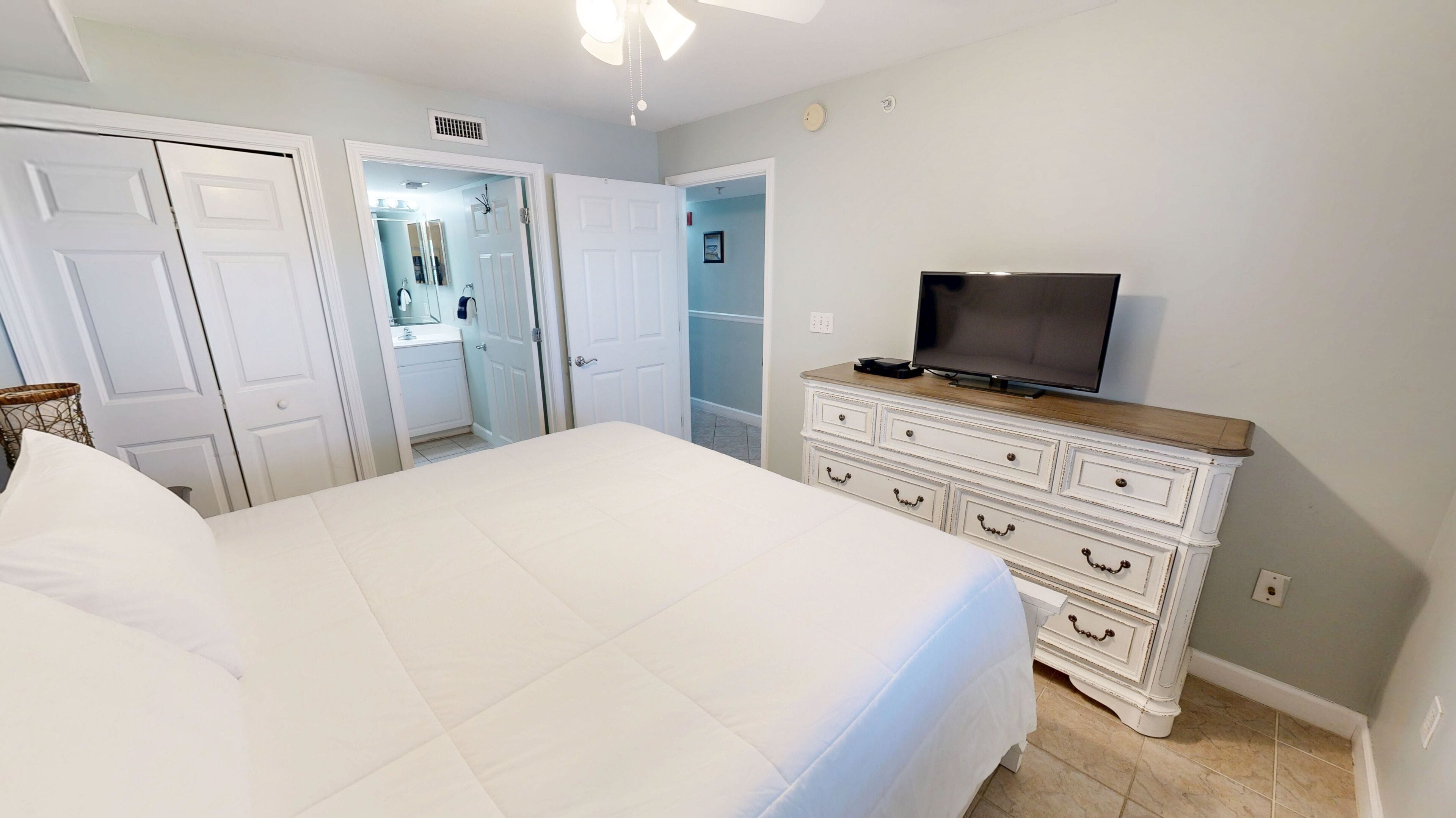 A bedroom with a bed, a dresser, a television, and a closet.