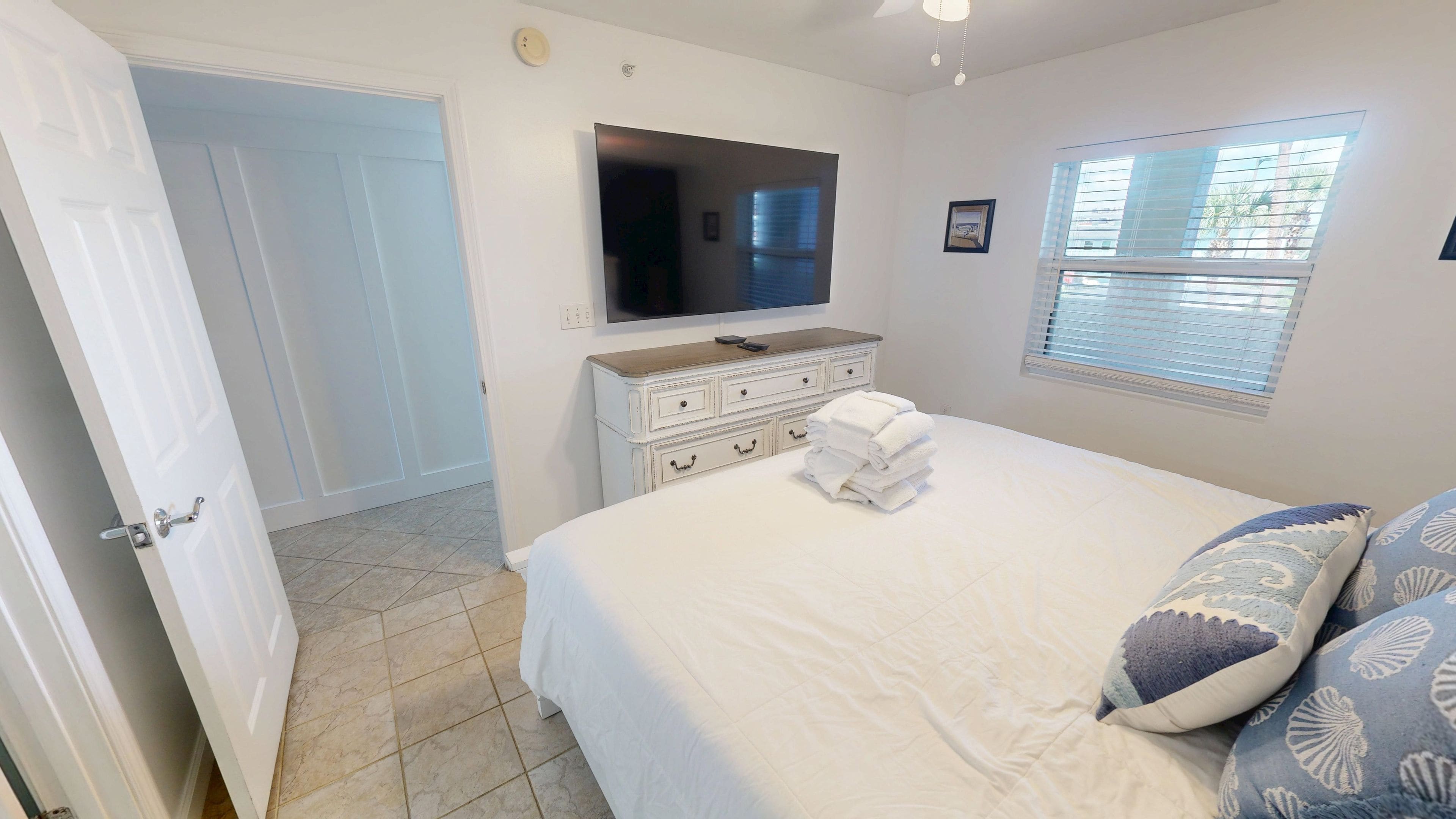 A bedroom with a bed, a dresser, a TV, and a window with blinds.