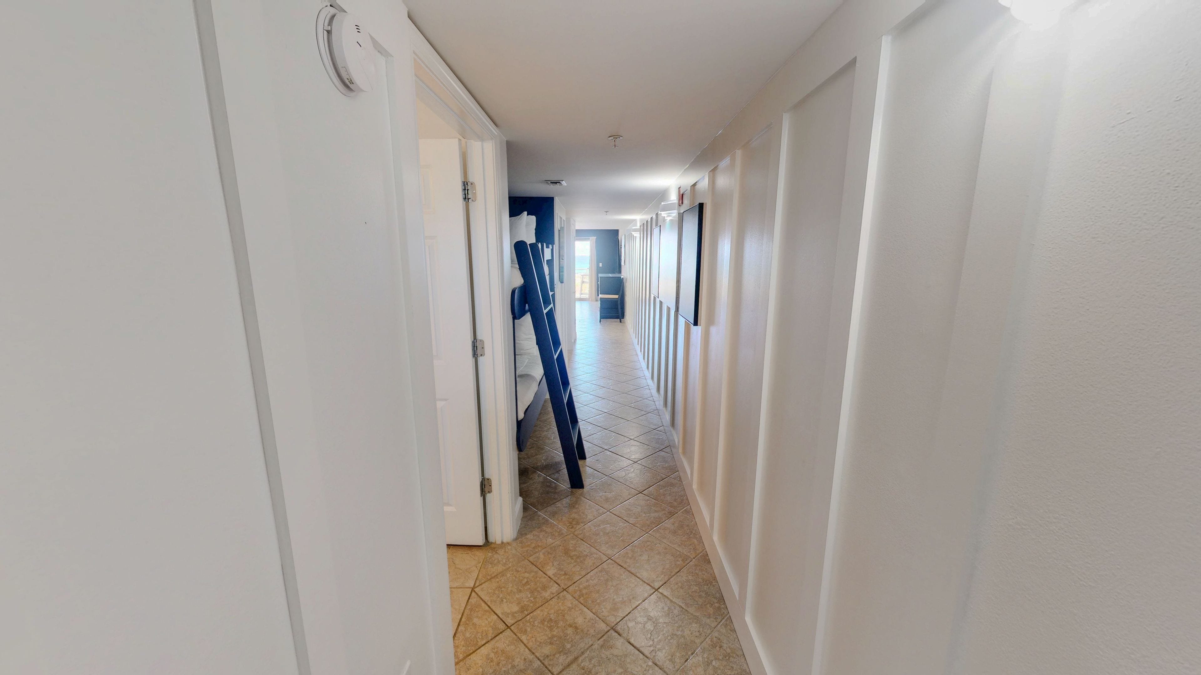 A hallway with white walls, a tiled floor, and a blue chair in the distance.