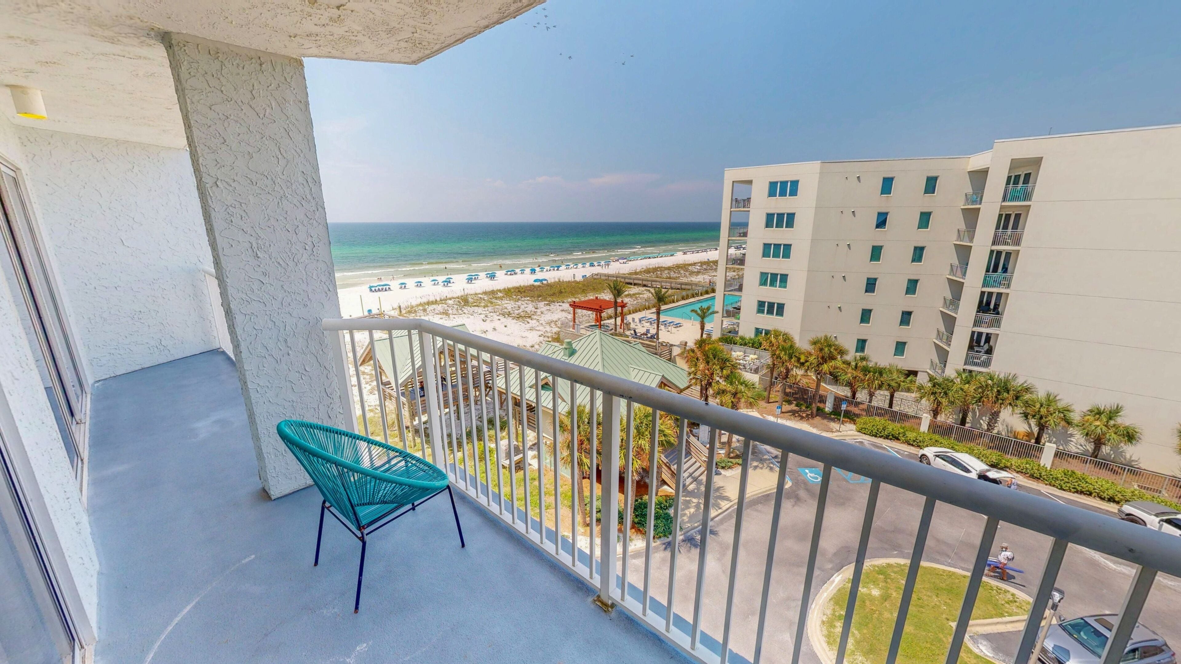 A balcony with a view of a beach, a pool area, and a multi-story building.