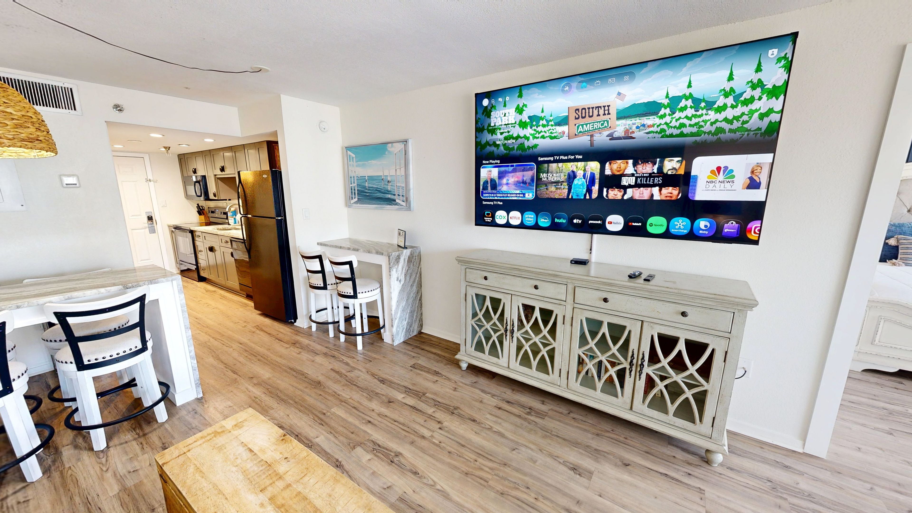 Eine moderne Küche mit Essbereich, einem großen Flachbildfernseher an der Wand und Holzboden.