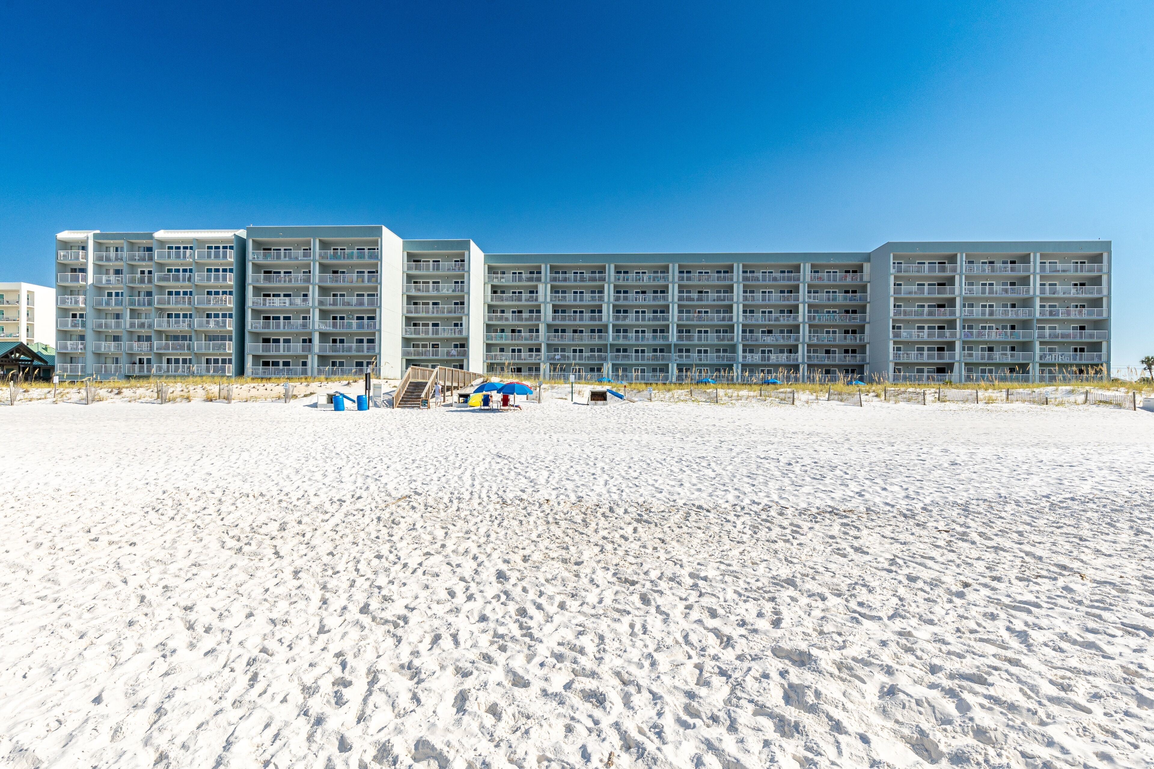 A beachfront hotel with multiple balconies, a sandy beach in front, and a clear blue sky.