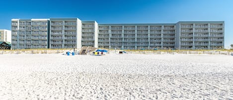 A beachfront hotel with multiple balconies, a sandy beach in front, and a clear blue sky.