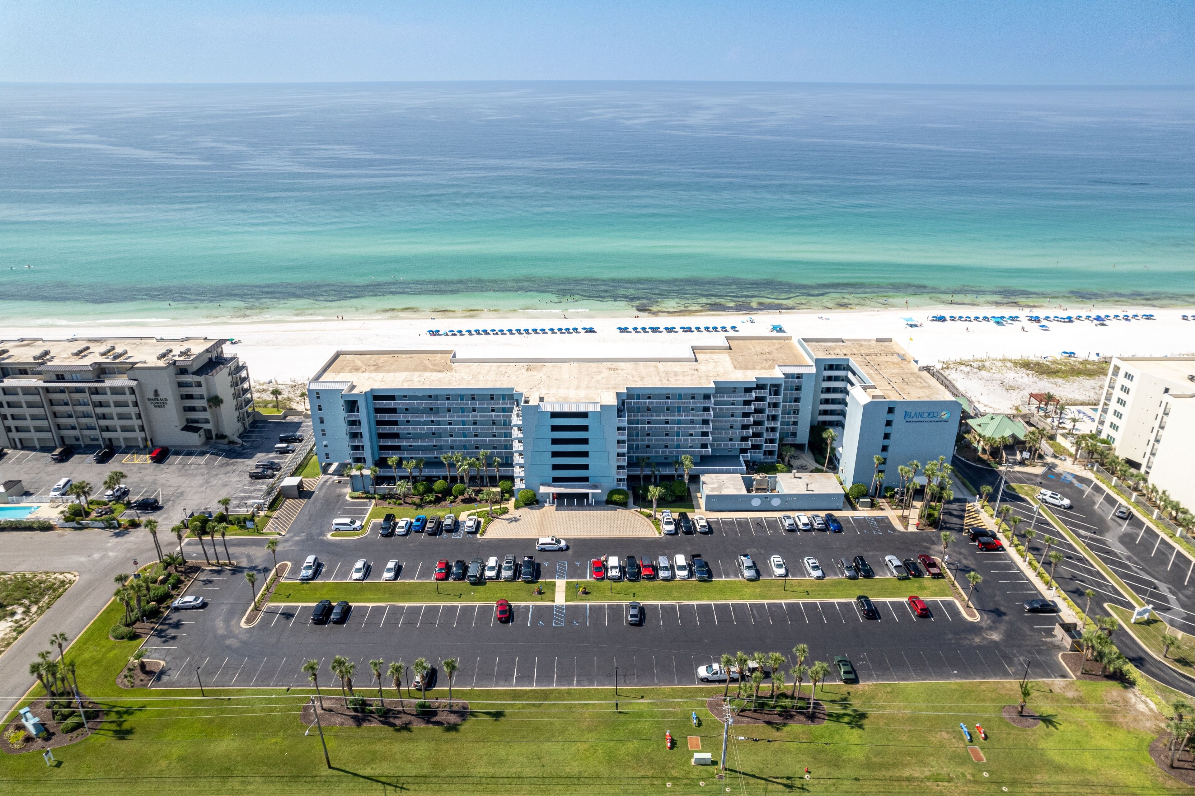 A hotel with a parking lot, a beach view, and a pool.