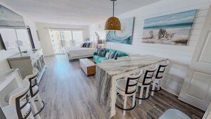 A modern living room with a marble coffee table, white bar stools, a teal sofa, and artwork on the walls. - Islander Beach Resort 0607 1 Bedroom Condo (Fort Walton Beach)