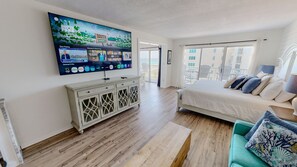A hotel room with a large TV mounted on the wall, a bed with multiple pillows, a white cabinet, and a balcony with a view. - Islander Beach Resort 0607 1 Bedroom Condo (Fort Walton Beach)