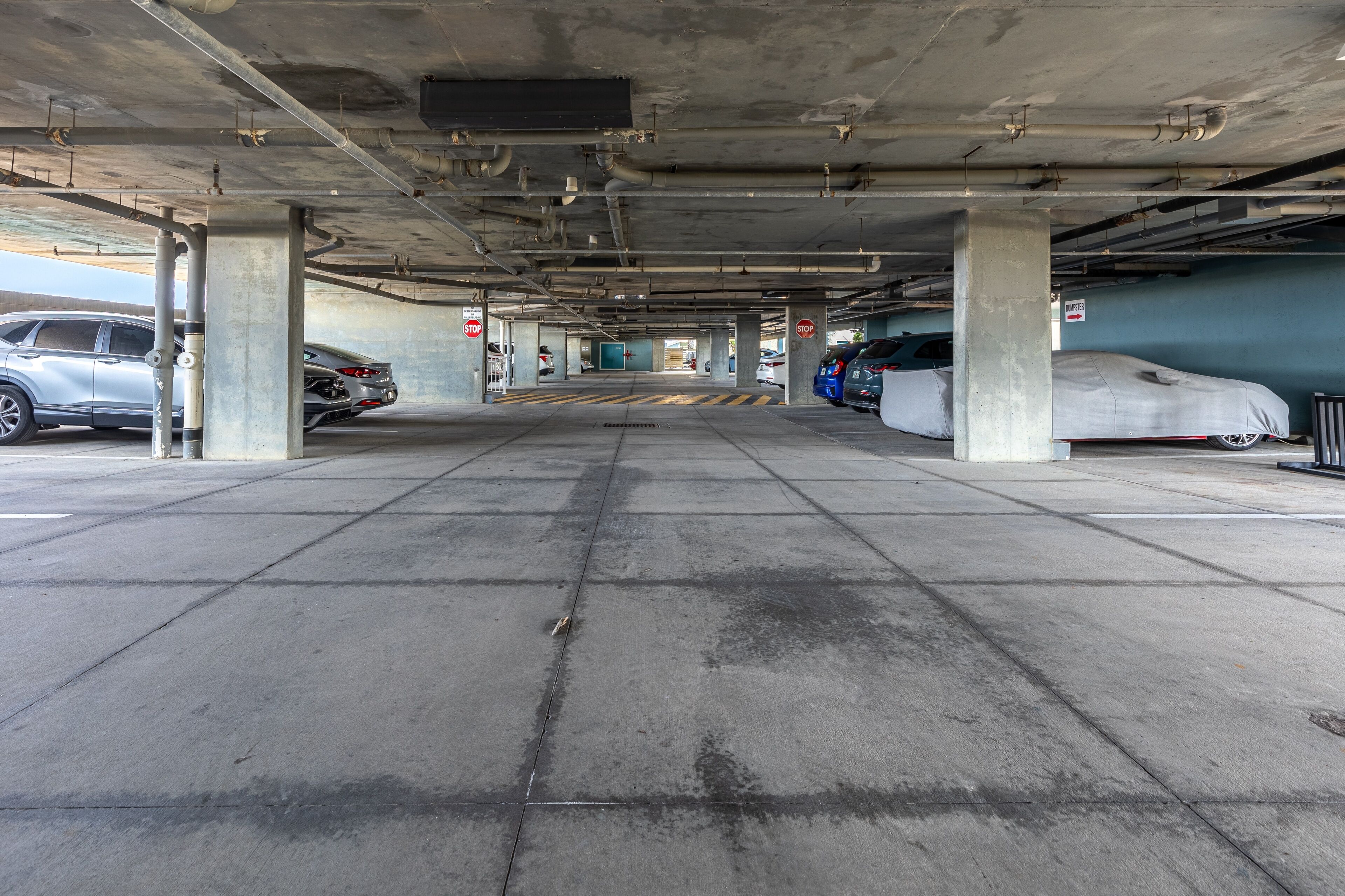 An underground parking garage with concrete pillars, a central walkway, and parked cars.