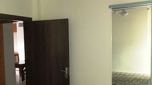 Une pièce avec un ventilateur de plafond, une porte en bois foncé, une cabine de douche en verre et une poubelle violette.