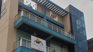 Un immeuble à plusieurs étages, sur lequel on peut lire l’enseigne « Urban Oasis Homestay », et dont la devanture, nommée « Plumeria M. », est bien visible.