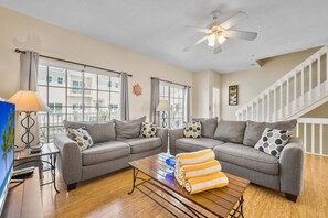 Ein Wohnzimmer mit zwei grauen Sofas, einem Couchtisch mit Handtüchern, einem Deckenventilator und einer Treppe.