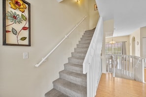 A staircase with a textured carpet and white handrail, leading to a landing with a white railing. - 1415 Gulf Dr N Holmes Beach, Anna Maria Island 3 Bedroom Townhouse (Bradenton Beach)