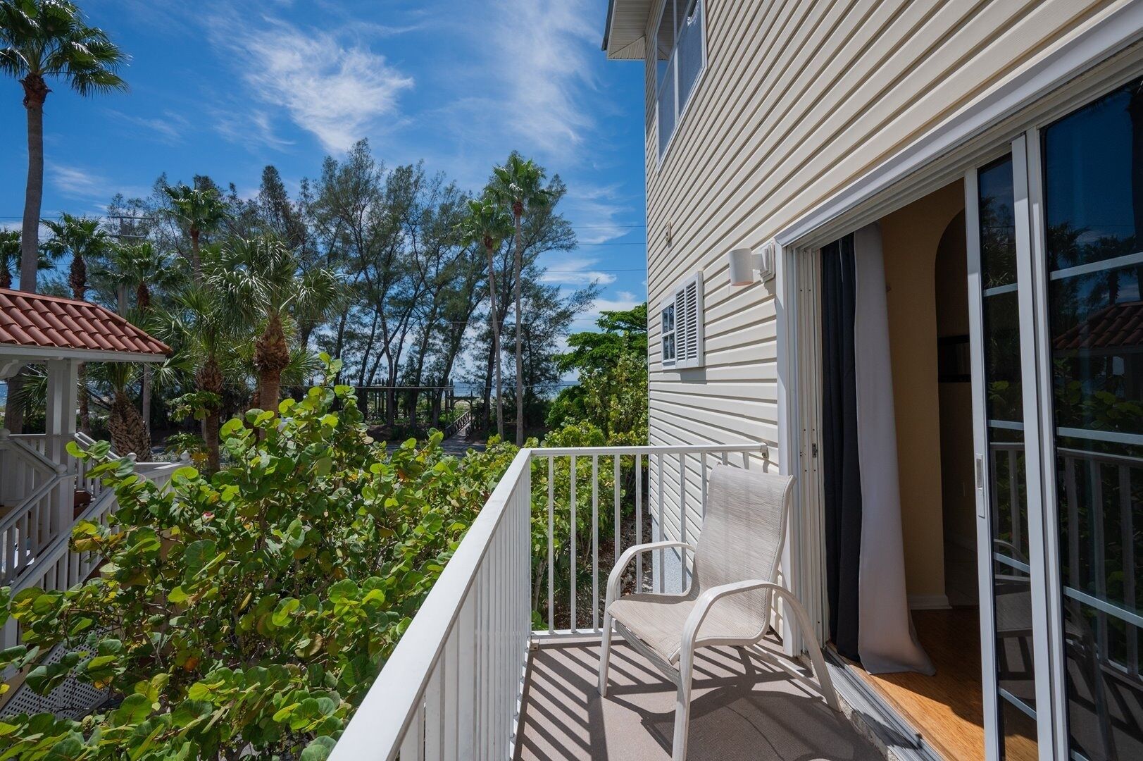 Una propiedad residencial con balcón, un patio cubierto y vista a un paisaje costero con árboles y cielo despejado.