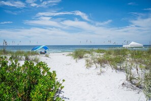 A beach with white sand, a blue and white tent, and a white canopy structure. - 1415 Gulf Dr N Holmes Beach, Anna Maria Island 3 Bedroom Townhouse (Bradenton Beach)