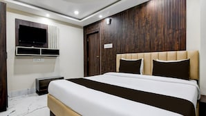 A modern bedroom with a large bed, a flat-screen TV mounted on the wall, and a wooden panel design on the wall behind the bed. - Classic With View Mivaan Comfort (Barasat)