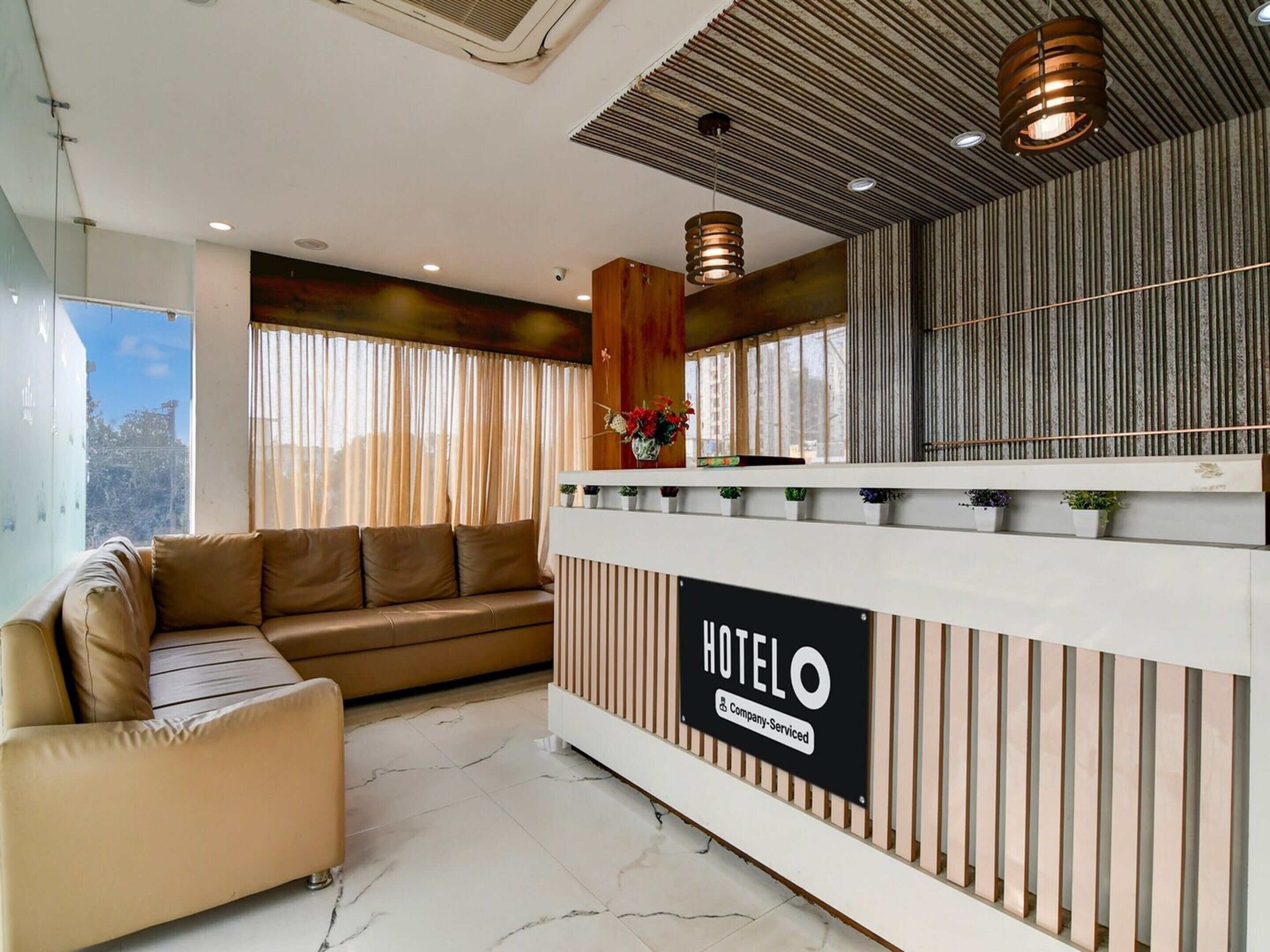A hotel reception area with a reception desk, a sofa, and a large window with curtains.