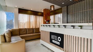 A hotel reception area with a reception desk, a sofa, and a large window with curtains. - Classic With View Mivaan Comfort (Barasat)