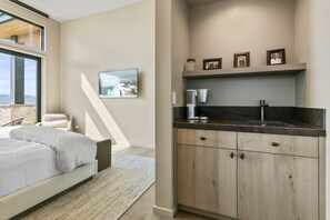 Un dormitorio moderno con una cama grande, vistas a un paisaje nevado a través de una ventana y una zona de cocina con estufa y armarios empotrados.