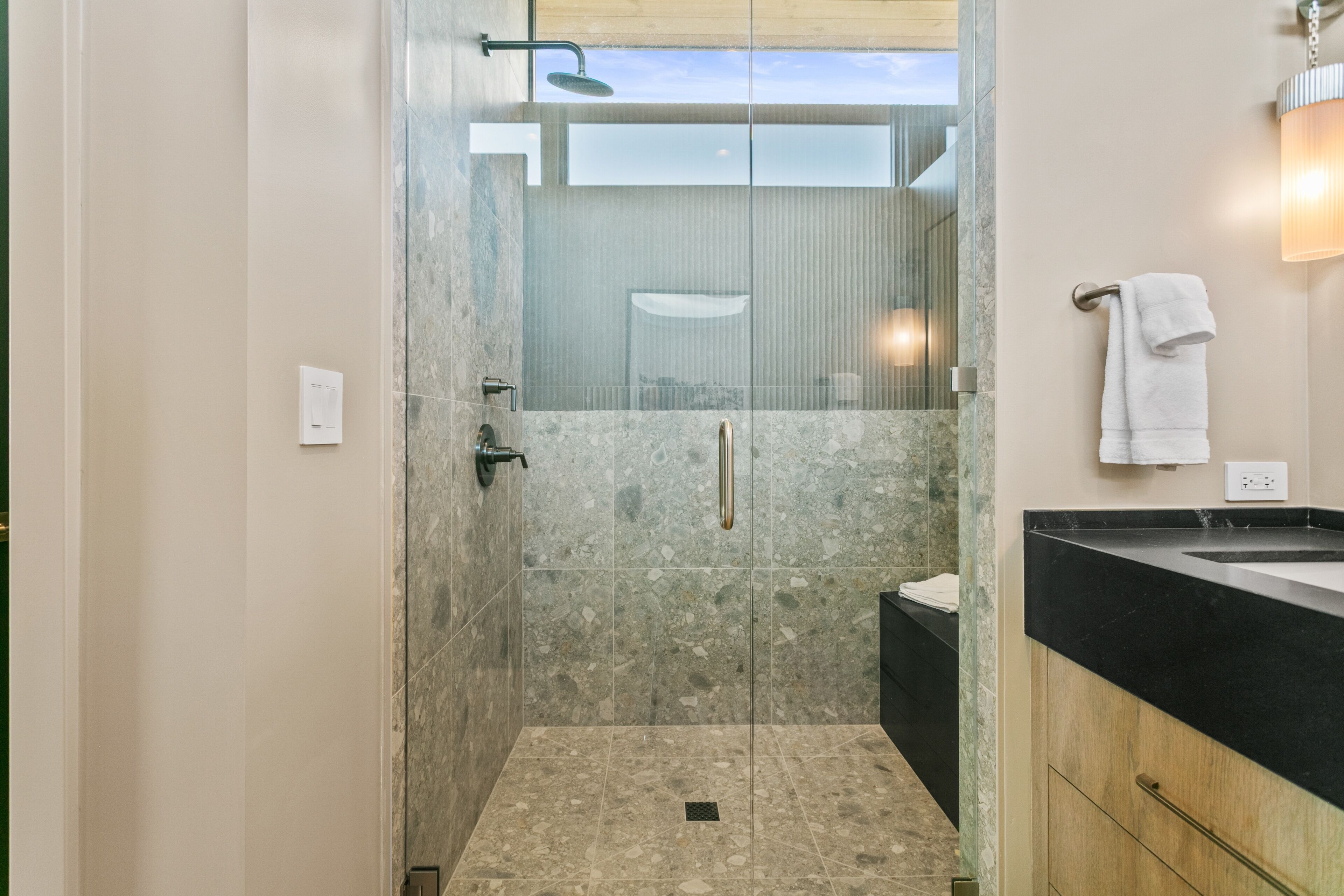 A modern bathroom with a glass-enclosed shower, a black countertop, and a towel rack.