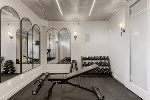 Een fitnessruimte met trainingsapparatuur, spiegels en gewichten.