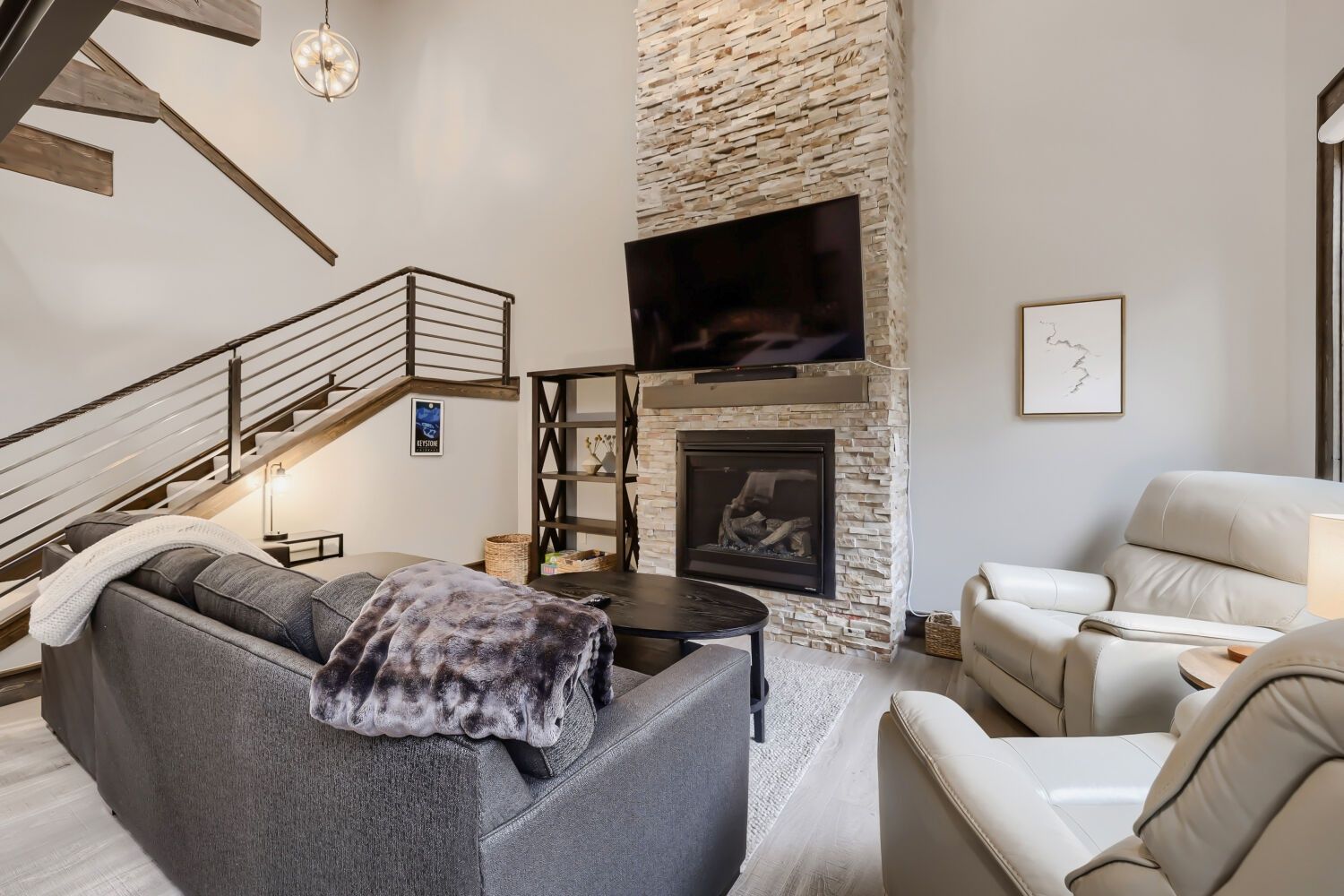 Una sala de estar moderna con chimenea de piedra, un televisor de pantalla plana, una escalera y un sofá.