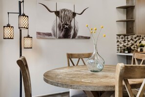 A dining area with a round wooden table, chairs, a glass vase with yellow flowers, and a wall-mounted artwork of a yak. - 1892 The Seasons 2 Bedroom Townhouse (Keystone)