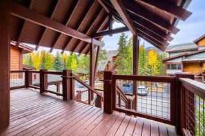 A wooden deck with a metal railing, overlooking a parking area and buildings with autumn foliage. - 1892 The Seasons 2 Bedroom Townhouse (Keystone)
