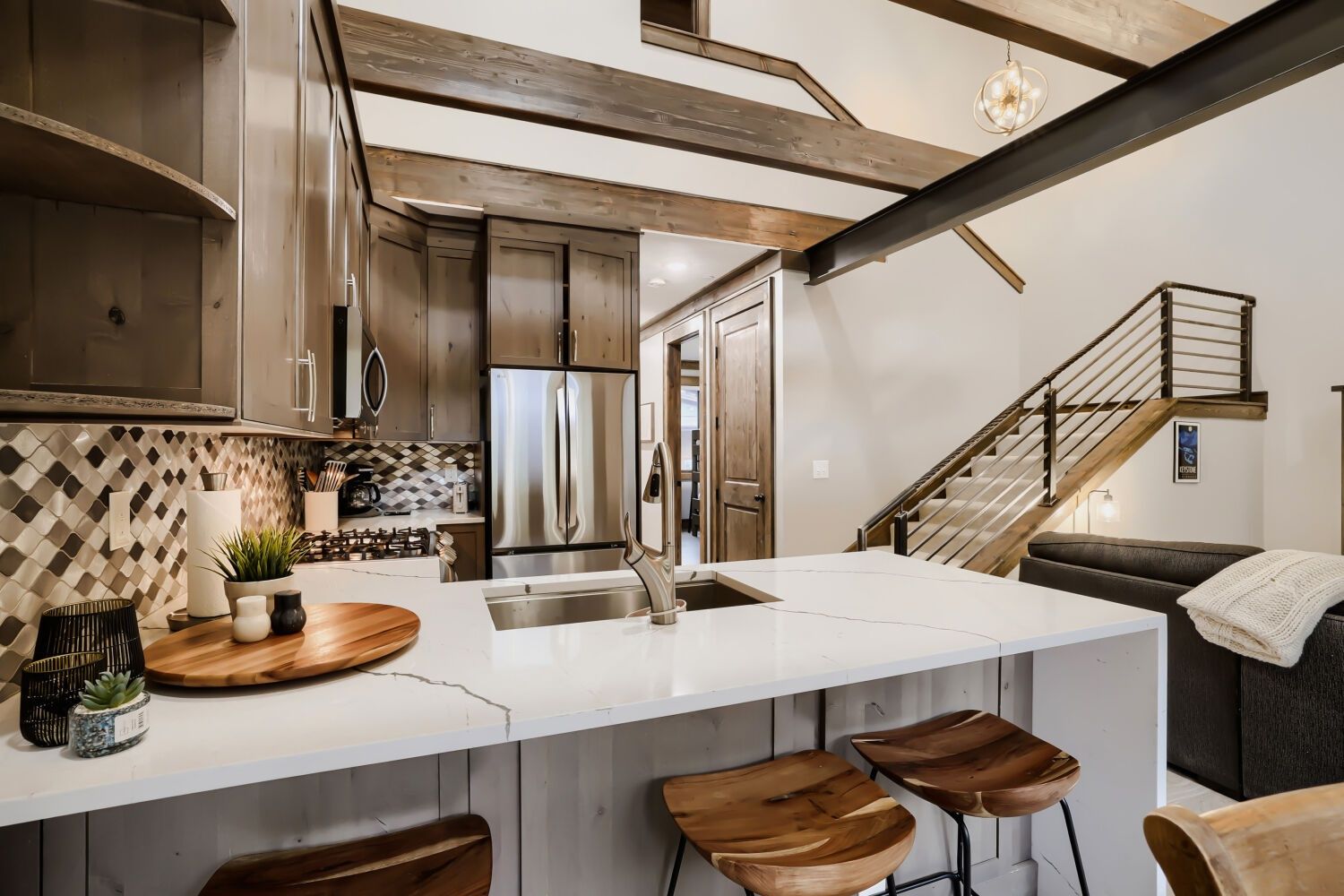 Una cocina moderna con una isla central, electrodomésticos de acero inoxidable y una escalera que sube a un nivel superior.
