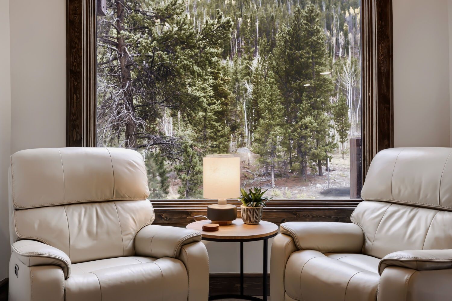 A room with two leather armchairs facing a window with a forest view.