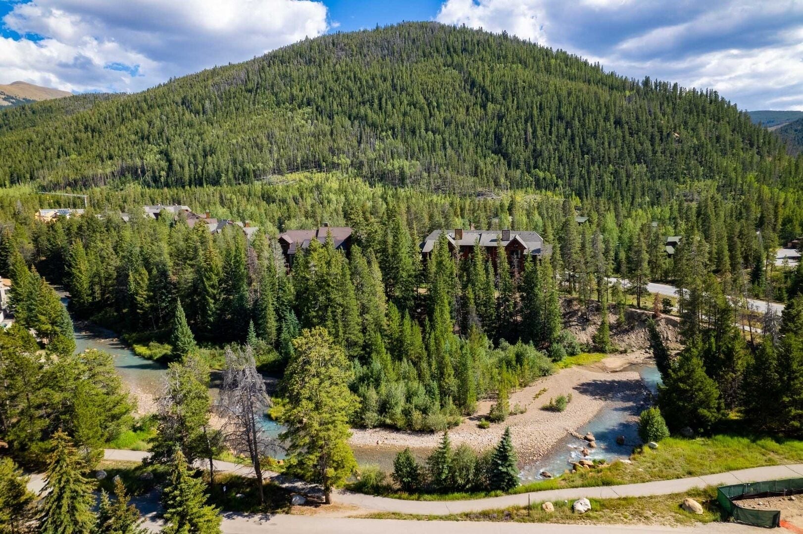 A mountainous area with a river, surrounded by dense forest and several buildings with dark roofs.