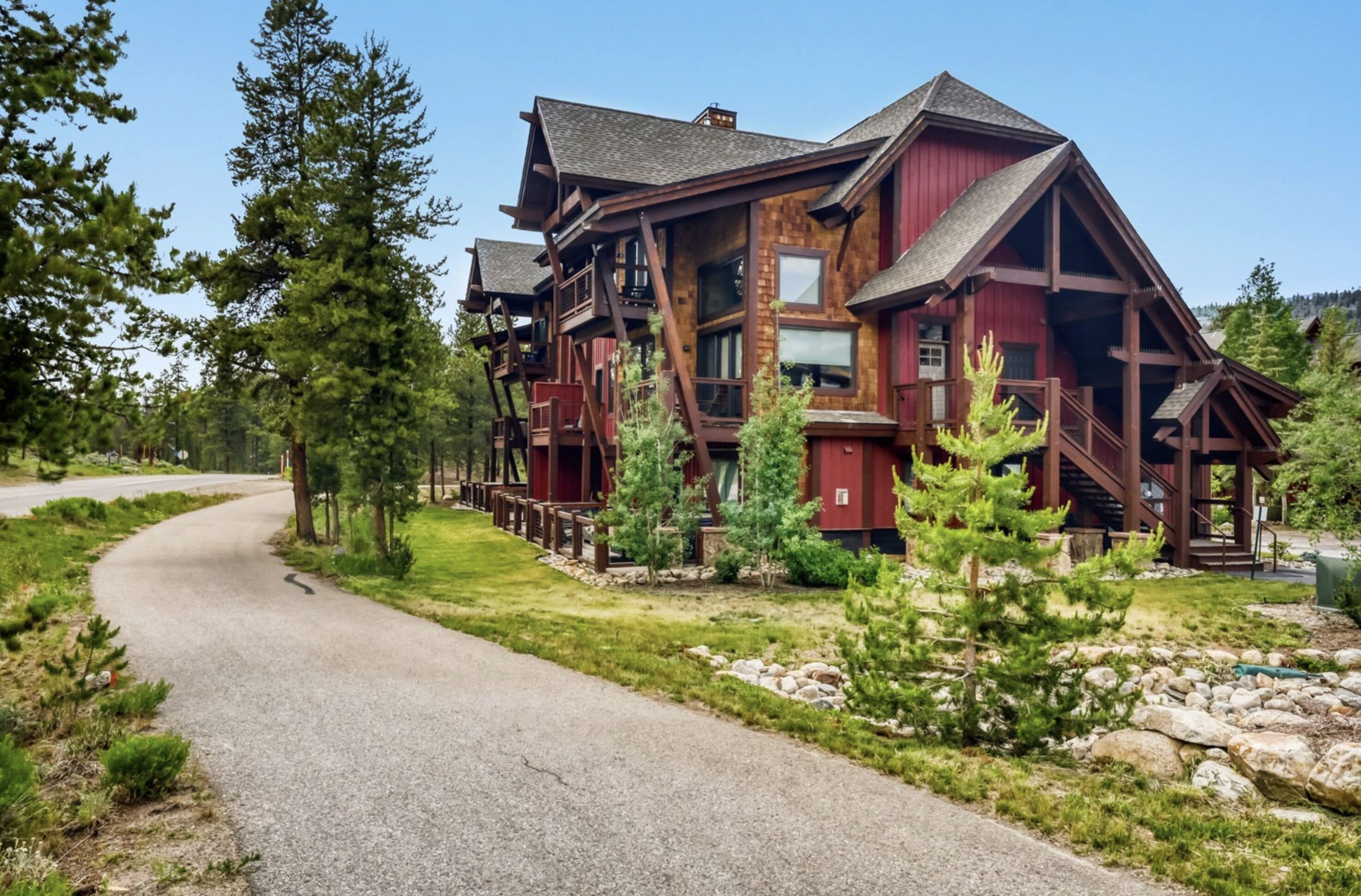 A multi-story lodge with a prominent wooden structure, a driveway leading to the entrance, and a surrounding landscape with trees and rocks.
