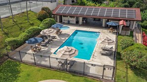 A swimming pool with lounge chairs and umbrellas, surrounded by a fence and greenery. - Kona Coffee Villas F153 2 Bedroom Condo (Holualoa)