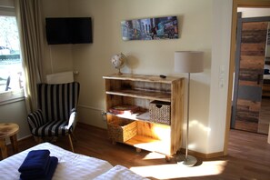 Une chambre d’hôtel avec un lit, une chaise à rayures, une étagère en bois sur laquelle se trouve un globe terrestre, une lampe et un tableau accroché au mur.