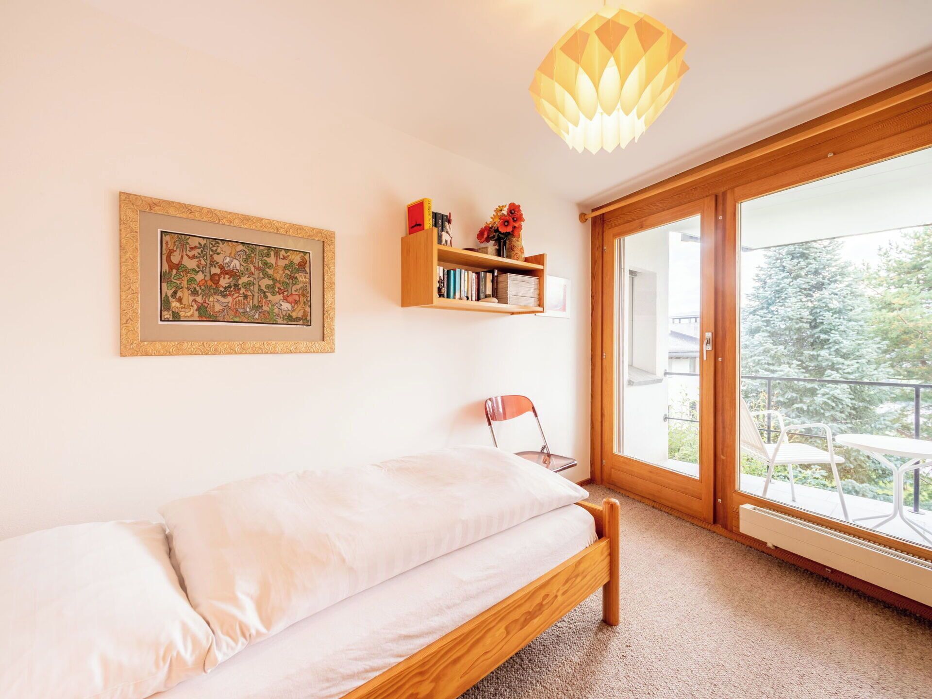 A bedroom with a bed, a bookshelf, a framed picture, and a view through a glass door.