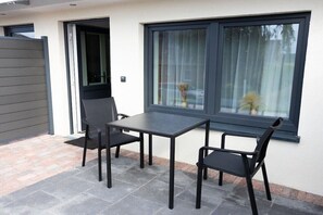 Une terrasse avec une table et des chaises, une porte coulissante et une fenêtre avec des rideaux.