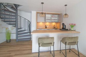 Eine moderne Küche mit einer zentralen Kochinsel, zwei Barhocker, einer eingebauten Ablage und einer Wendeltreppe.