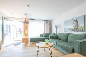 Un salon moderne avec un canapé vert, une table basse ronde et un tableau représentant un moulin à vent accroché au mur.