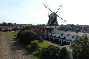 Eine Windmühle neben einem modernen Gebäude mit flachem Dach und einem weitläufigen Feld im Vordergrund.