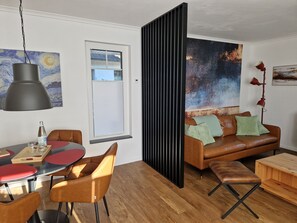 Ein modernes Wohnzimmer mit einer braunen Ledersofa, einem Esstisch mit Stühlen, einem großen abstrakten Gemälde und einer schwarzen Trennwand.