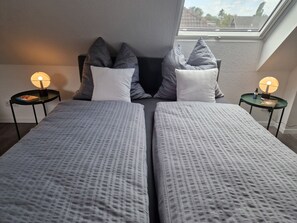 Een slaapkamer met twee bedden, grijze beddengoed, twee nachtkastjes met lampen en een dakraam.