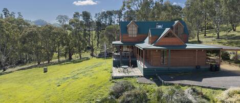 Une cabane en bois avec un toit vert, entourée d’un champ herbeux et d’arbres.