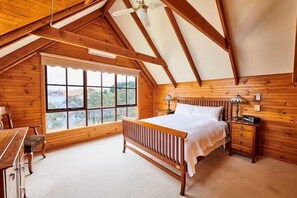 Een slaapkamer met een houten plafond, een groot raam, een bed, nachtkastjes en een bureau.