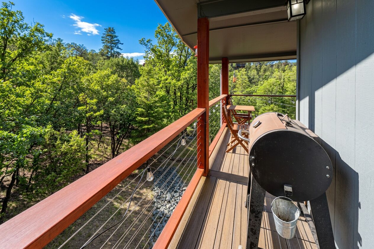 Un balcón con una parrilla y un cubo de metal, con vista a una zona boscosa.