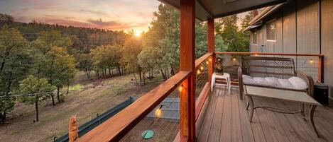 A wooden deck with a bench and a table, overlooking a forested area.