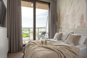 Un dormitorio con una cama grande, vistas de la ciudad desde un balcón y una silla afuera.