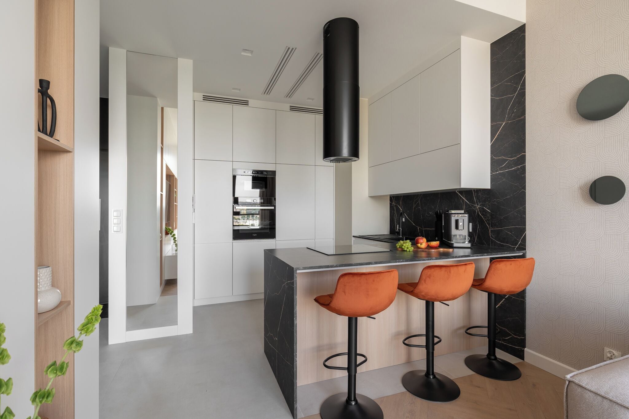 A modern kitchen with a central island, bar stools, and a black range hood.