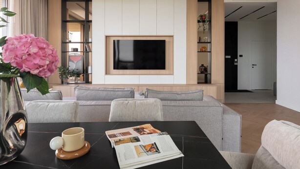 A modern living room with a flat-screen TV, grey sofas, a coffee table with a magazine, and a vase with pink flowers. - Bulvar Penthouse Collection Gdańsk (Gdańsk)