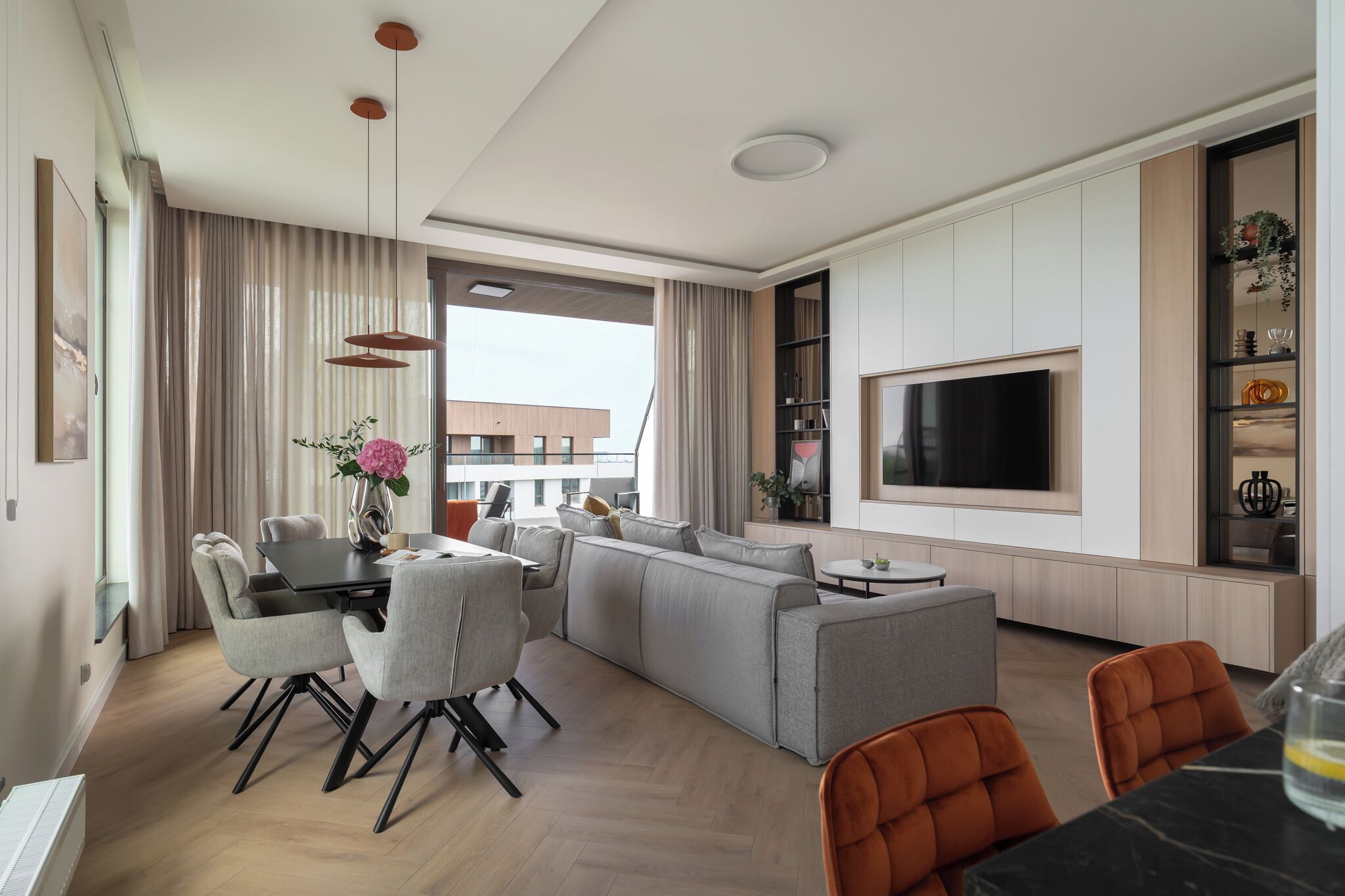 A modern living room with a sofa set, dining area, and a TV mounted on the wall.
