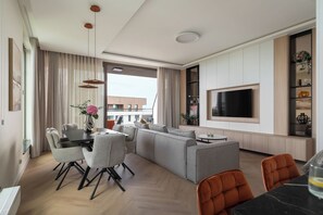 A modern living room with a sofa set, dining area, and a TV mounted on the wall.