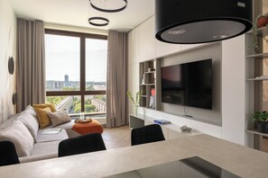 A modern living room with a sofa, dining table, and a large TV. - Bulvar Penthouse Collection Gdańsk (Gdańsk)