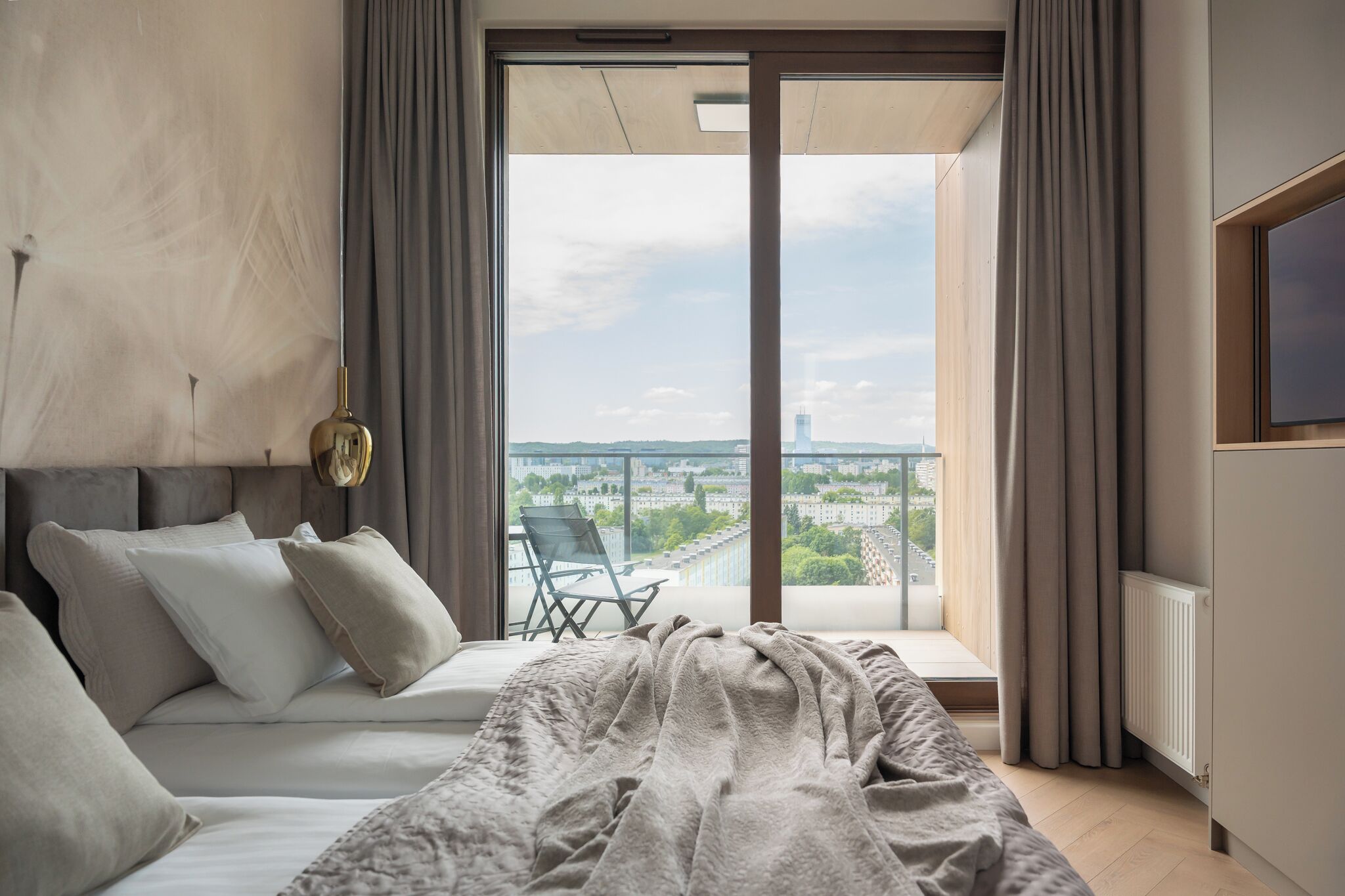 A modern bedroom with a large bed, a balcony with a view of the city, and a chair.
